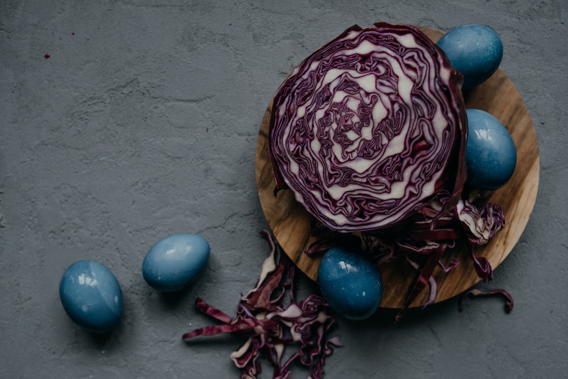 a red cabbage and blue eggs on a wooden chopping board