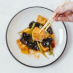 a person holding chopsticks with tofu